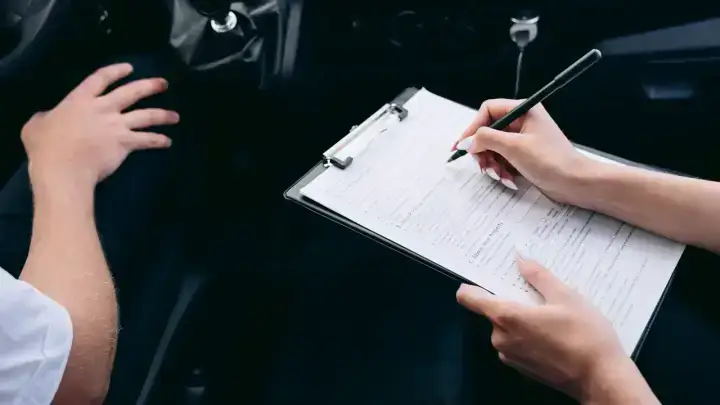 Driver reviewing insurance paperwork on a clipboard inside a car before restoring auto coverage