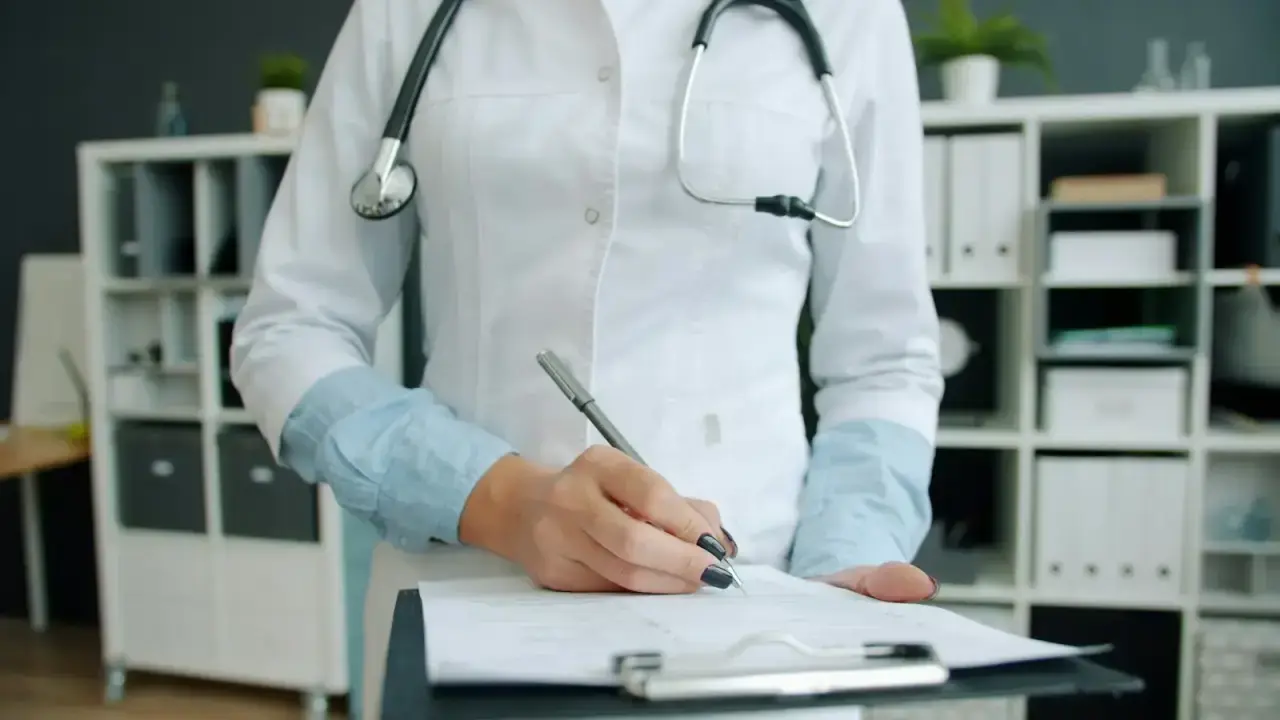 Doctor writing on medical paperwork illustrating how consumers compare health insurance premiums, deductibles and out-of-pocket costs