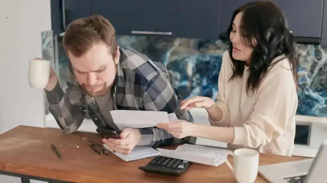 Couple reviewing household bills with a calculator and laptop illustrating health insurance premium payment decisions