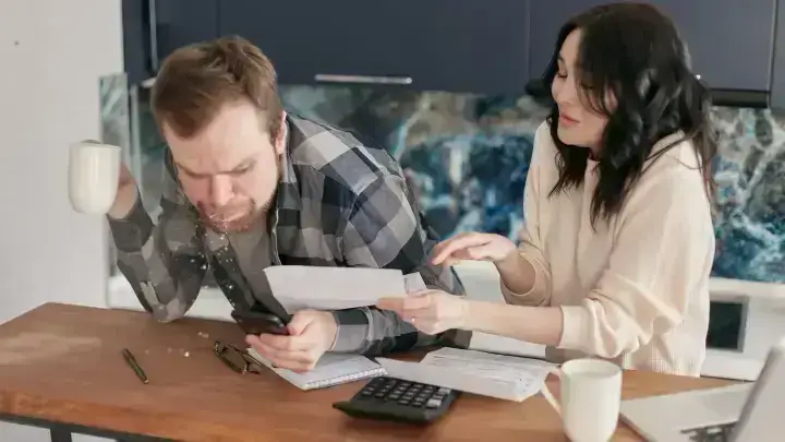 Couple reviewing household bills with a calculator and laptop illustrating health insurance premium payment decisions