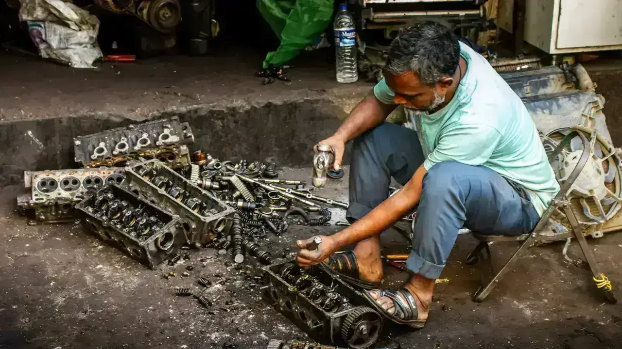 Mechanic working on automobile engine parts, illustrating OEM and aftermarket replacement-part choices after an insured crash